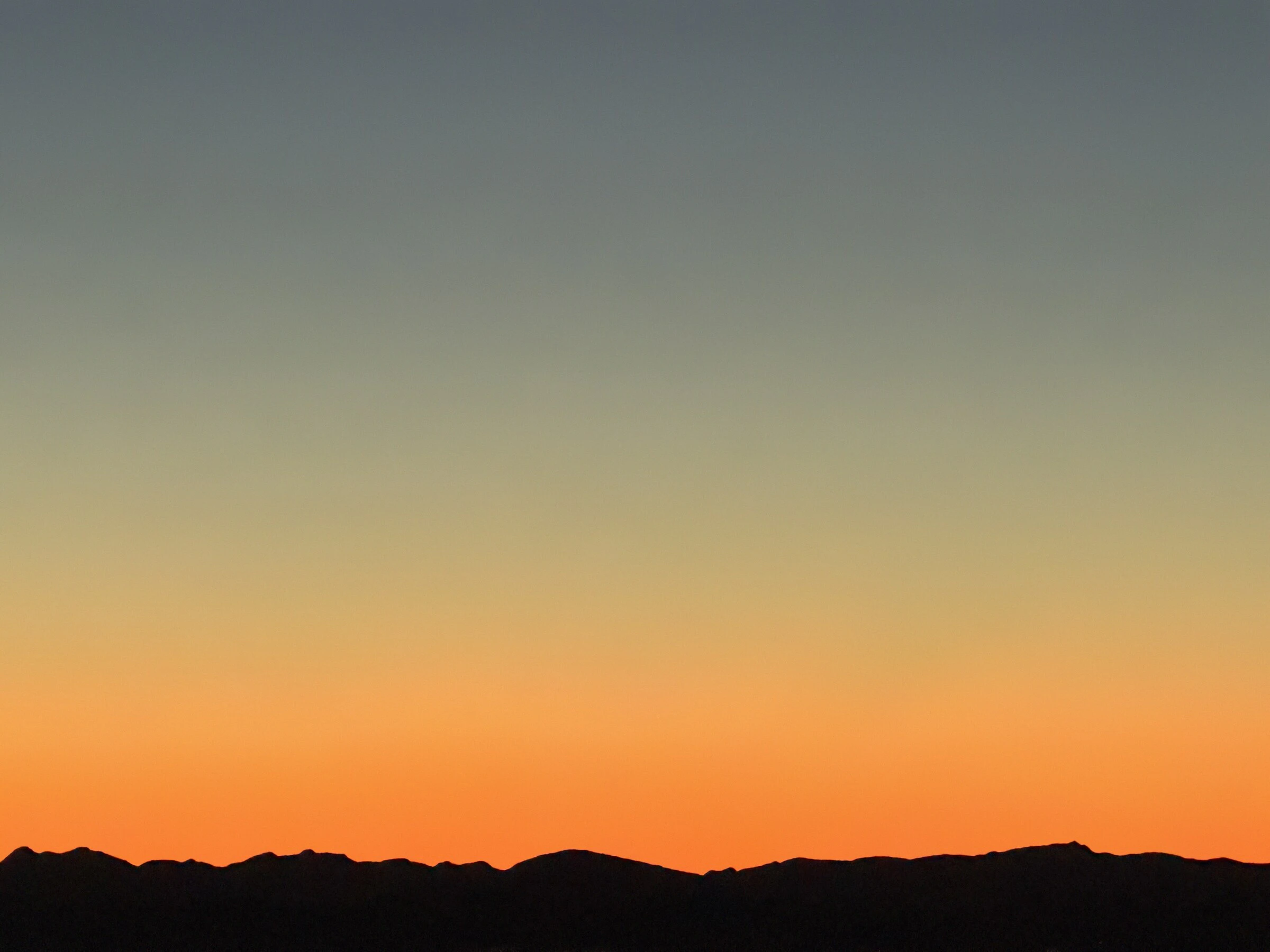 The North Shore mountains in silhouette against an orange sunset sky